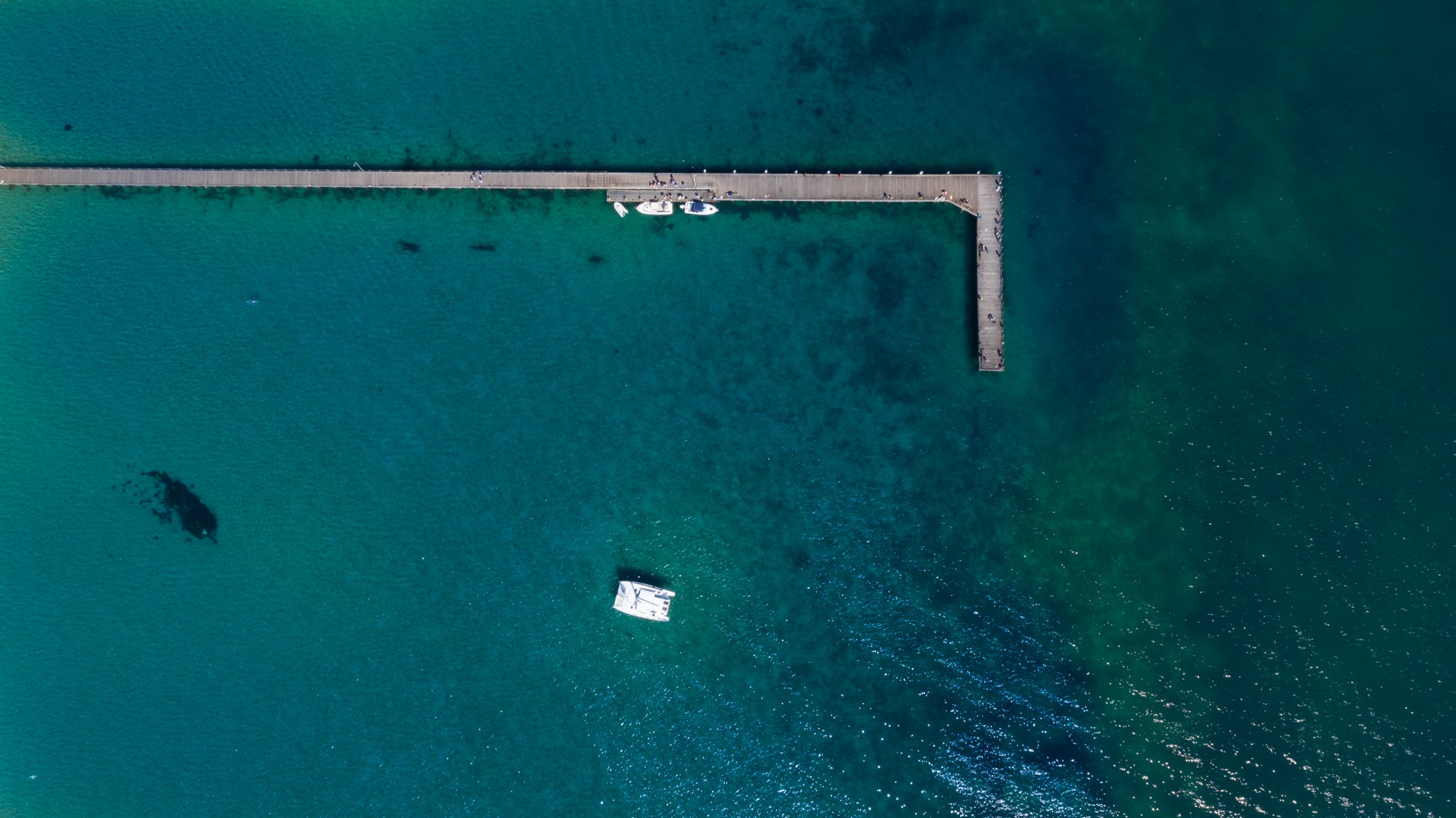 Overhead picture of a dock with boats at it and one anchored out.